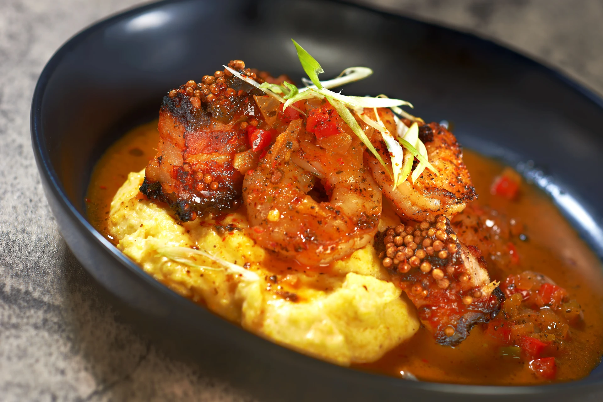 Pastrami Style Campus Pork Belly, Blackened Shrimp, Creamy Edwards Mill Yellow Grits, Garlic-Herb Butter Sauce, and Scallions